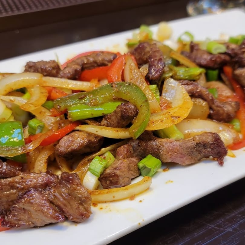 Indian beef stir-fry with green and red bell peppers, onions, and scallions on a white plate.