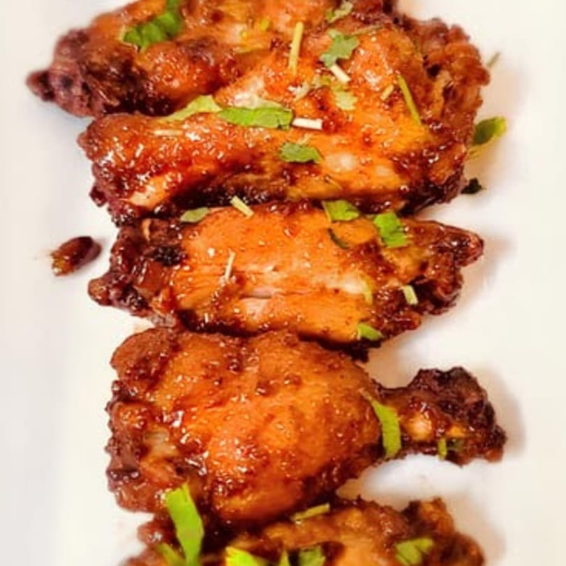 Close-up of five glossy, dark brown chicken wings garnished with fresh green herbs on a white plate.